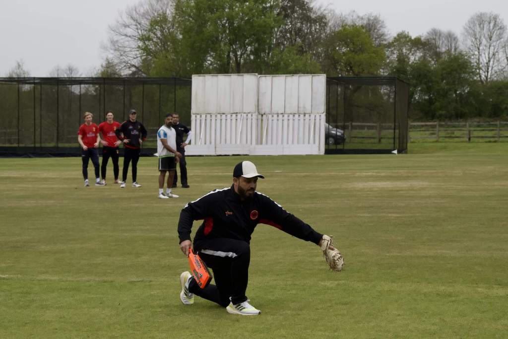 Cricket coach demonstrating a fielding drill during a practical coaching workshop on a cricket outfield.